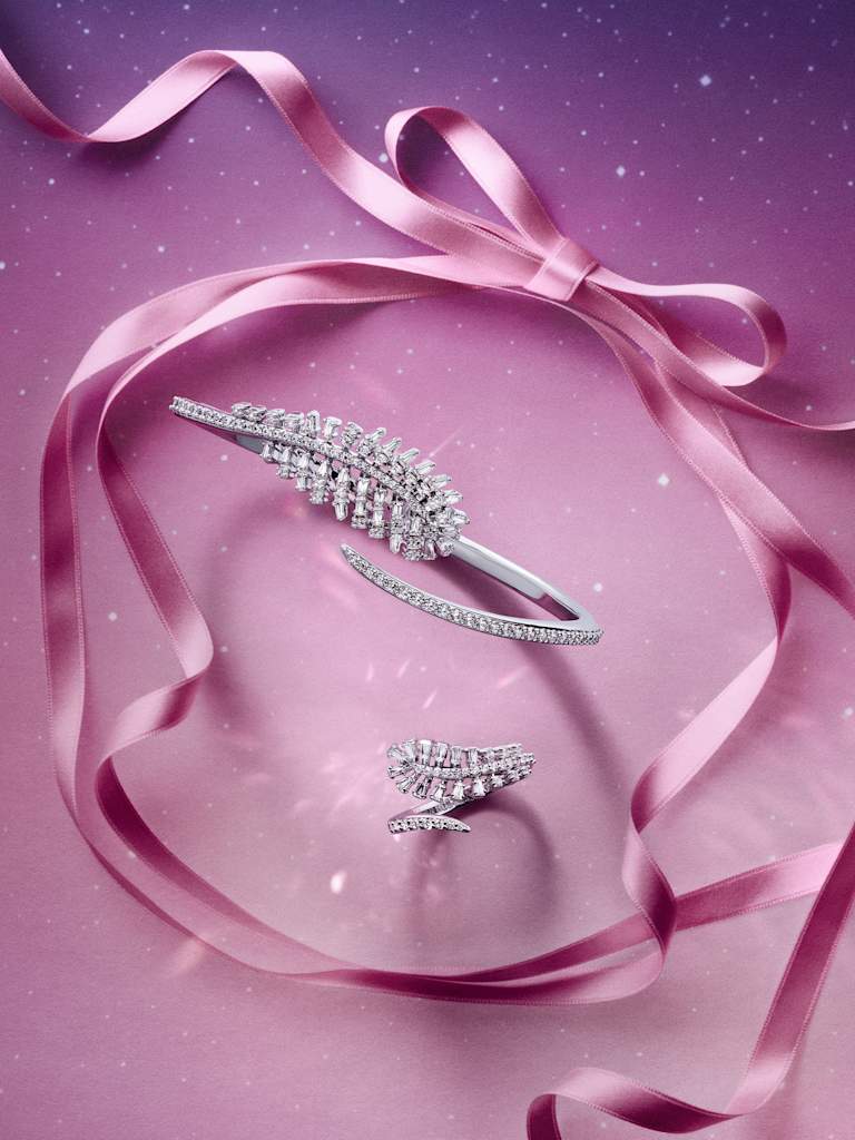 Swarovski clear crystal feather bangle and ring displayed with pink ribbon on a starry background.
