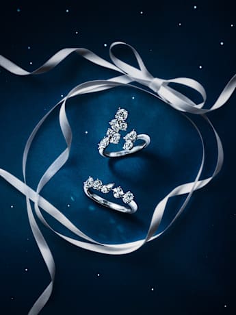 Two Swarovski Galaxy crystal rings displayed with white ribbon on a dark blue background.
