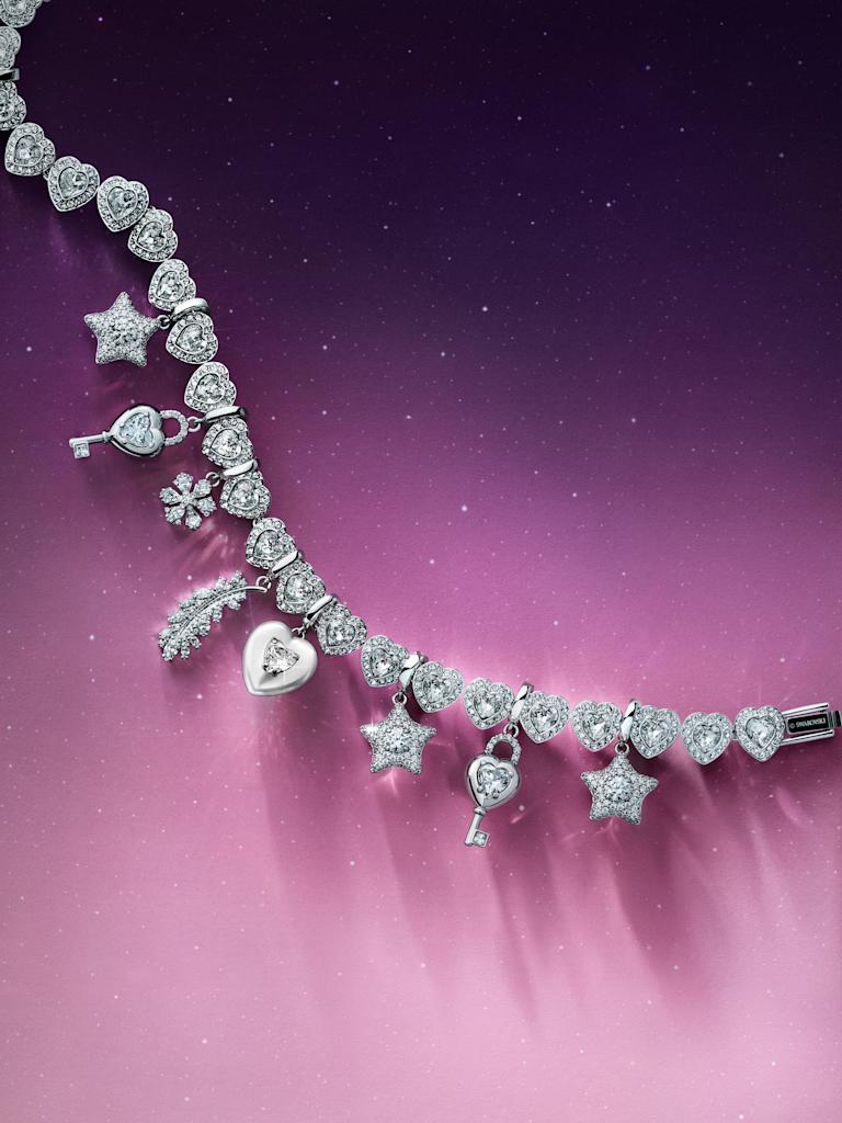 Swarovski clear crystal charm bracelet with heart, star, and key charms on pink background.