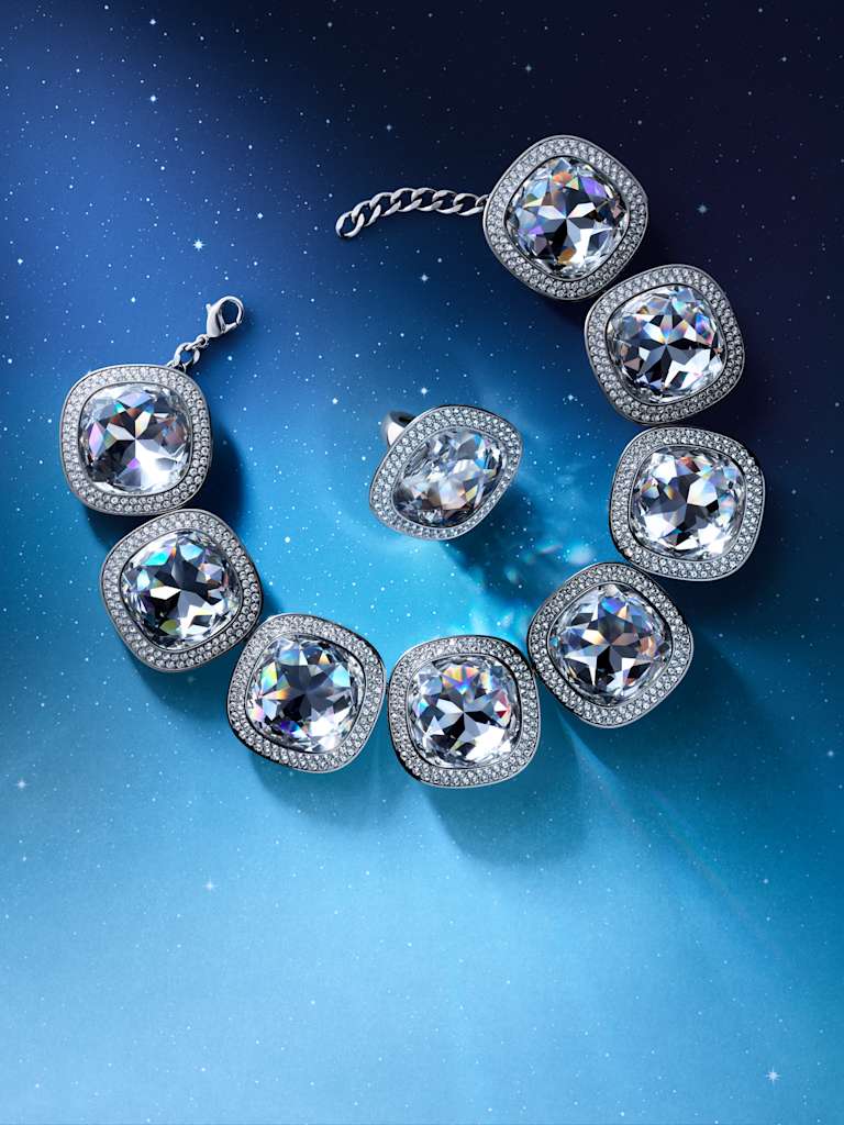 Swarovski Una Angelic crystal bracelet and matching ring arranged on a blue starry background.