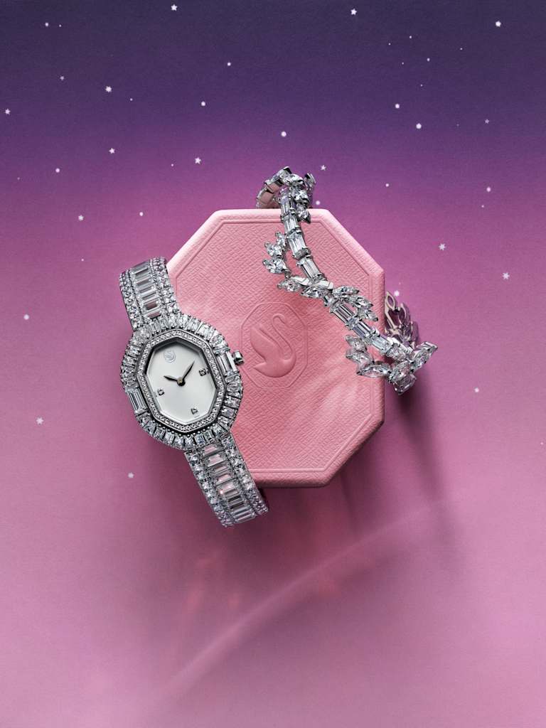 Swarovski crystal watch and ring displayed on a pink gift box against a starry background.