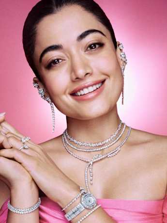 Female model in pink top wearing  Swarovski clear crystal earrings, layered necklaces, rings, and bracelets.