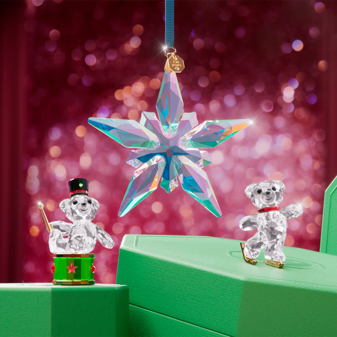 Figurky Medvídek Kris od Swarovski na zelených dárkových krabičkách Swarovski s Annual Edition Ozdoba zavěšenou nad nimi Figurky Medvídek Kris od Swarovski na zelených dárkových krabičkách Swarovski s Annual Edition Ozdoba zavěšenou nad nimi