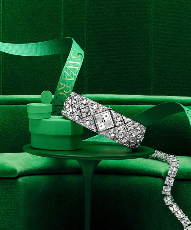 Hodinky a šperky Swarovski se zelenou dárkovou krabičkou uložené na zeleném stole se zeleným pozadím Hodinky a šperky Swarovski se zelenou dárkovou krabičkou uložené na zeleném stole se zeleným pozadím