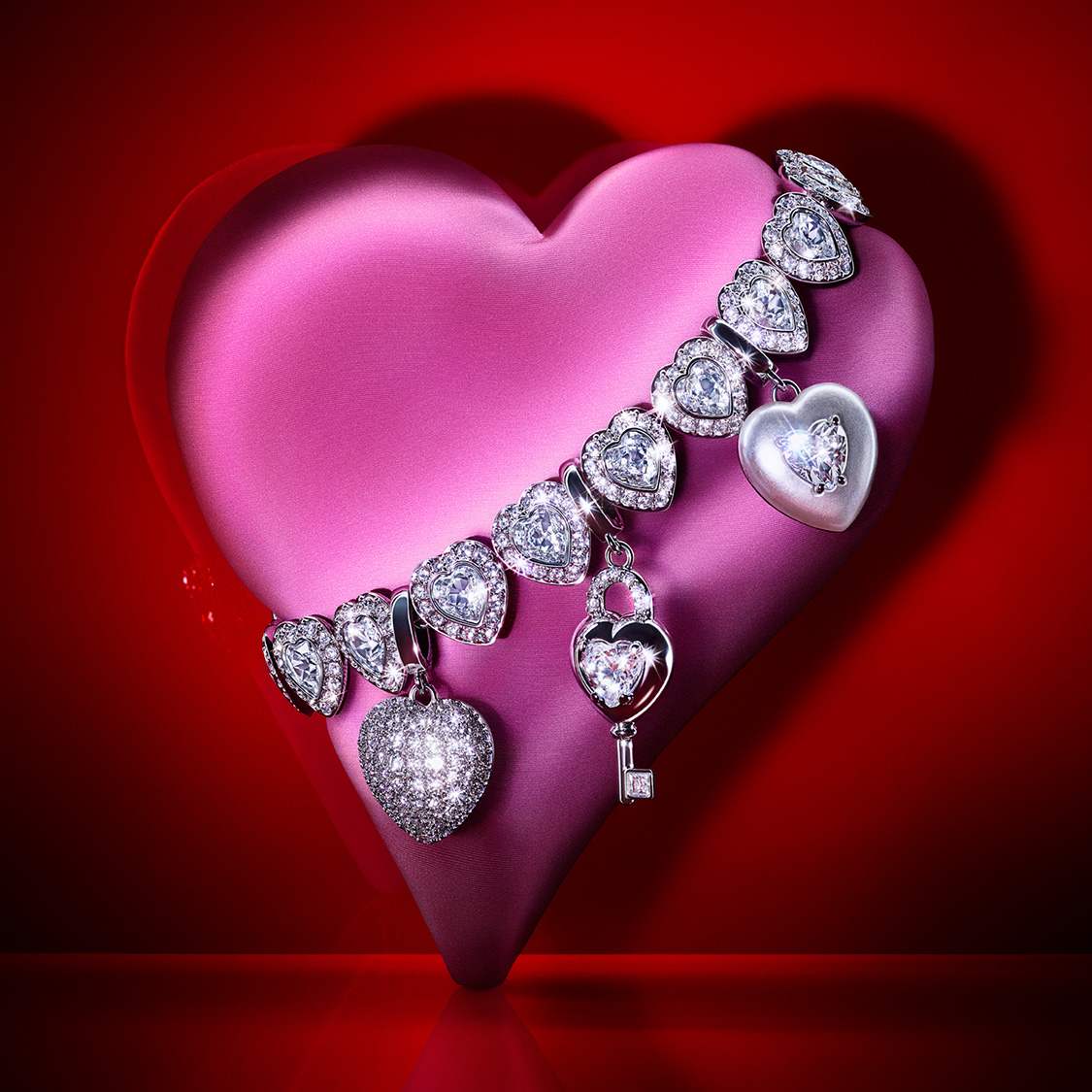 A pink heart has a Swarovski bracelet draped over it with several Swarovski Charms attached
