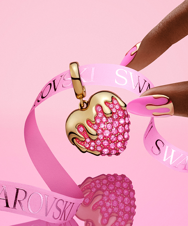 Palce sięgające po przywieszkę w kształcie serca na różowym tle