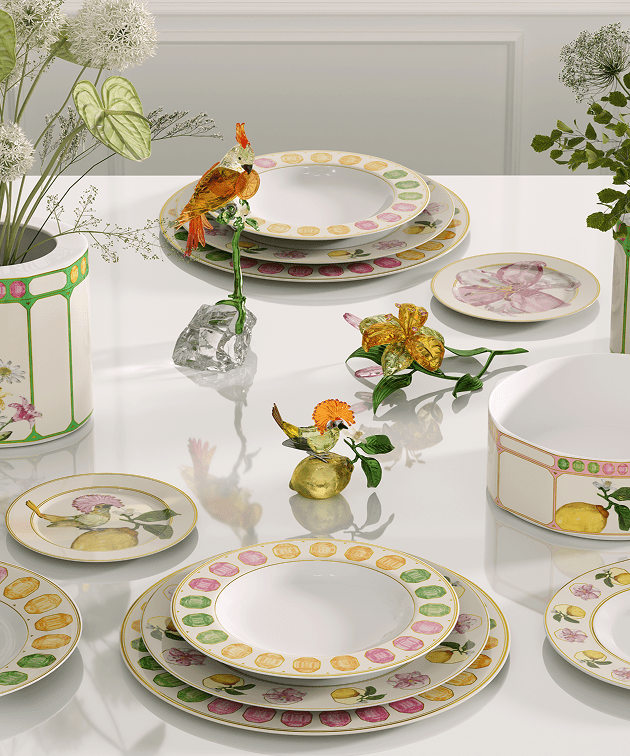 Jídelní stůl prostřený talíři z kolekce Swarovski x Rosenthal a zdobený jasnými, pestrobarevnými květy a zvířecími figurkami z Křišťálu Swarovski