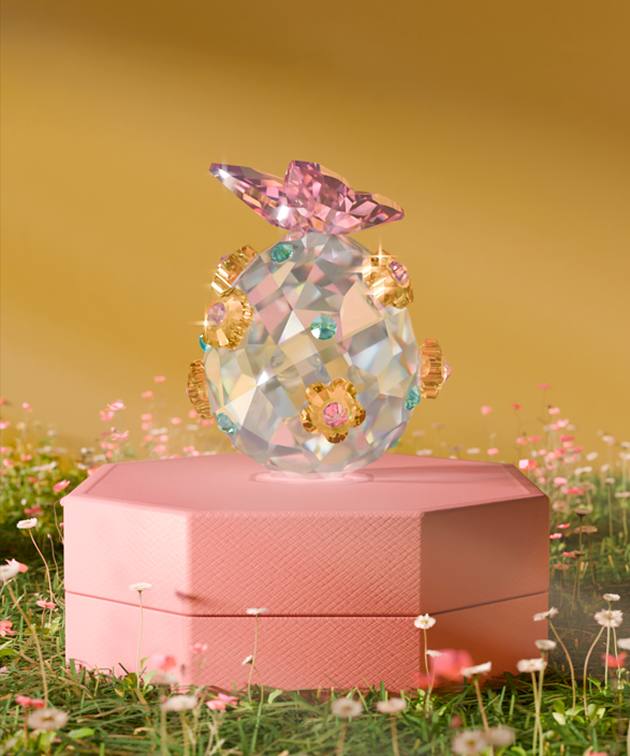 Jajko z oszlifowanego kryształu Swarovskiego ozdobione różowymi, niebieskimi i złotymi akcentami, zwieńczone motylem z różowego kryształu Swarovskiego.